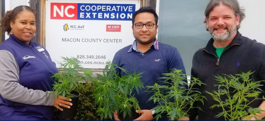 Three individuals holding plants in front of an N.C. Cooperative Extension logo banner