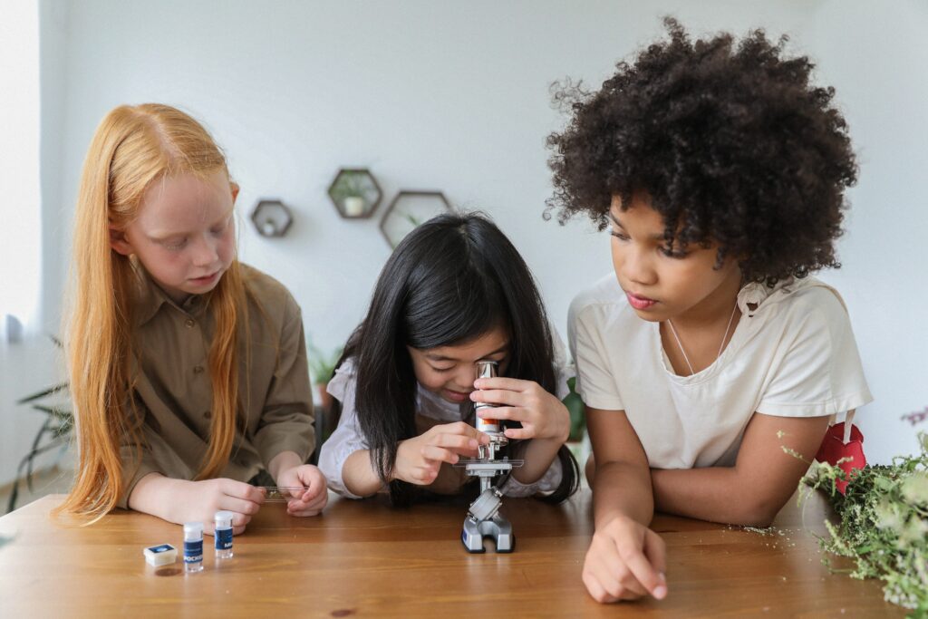 Three girls hovered over a microscope