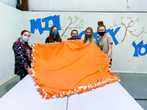 5 children standing with a large orange blanket in front of them.