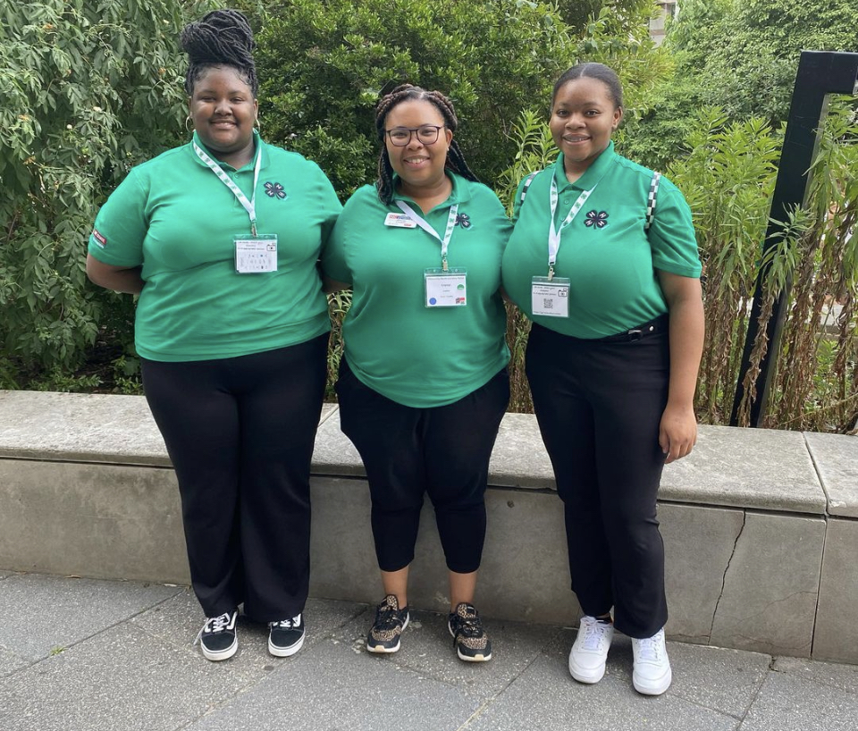 Three young women in green 4-H shirts standing together.