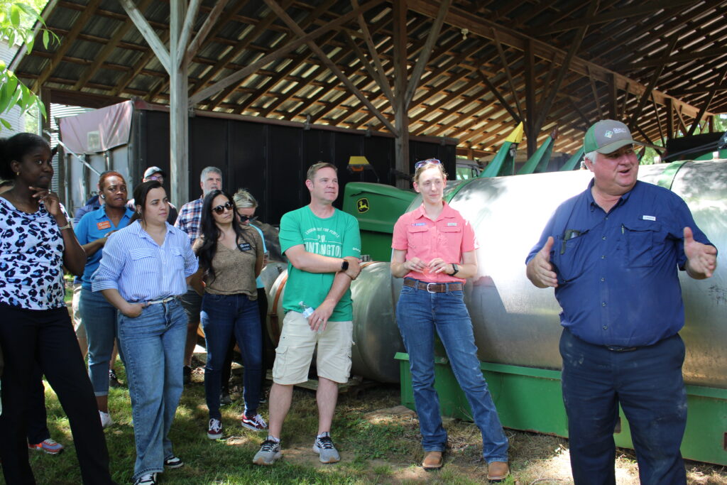 Farmer Randy Baucom speaking to attendance in front of large farm machinery used on row crops.